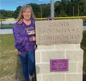 Woman posing with the Cathedral Latin School 1929 annex cornerstone at NDCL Lion Stadium